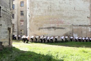 Menschen in gebückter Haltung auf Wiese vor einer Mauer