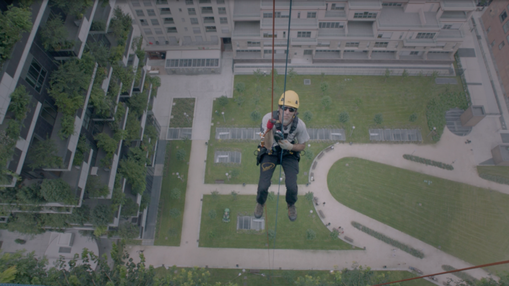 Person secured to a cable, hanging beside a building