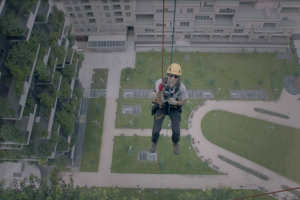 Person secured to a cable, hanging beside a building