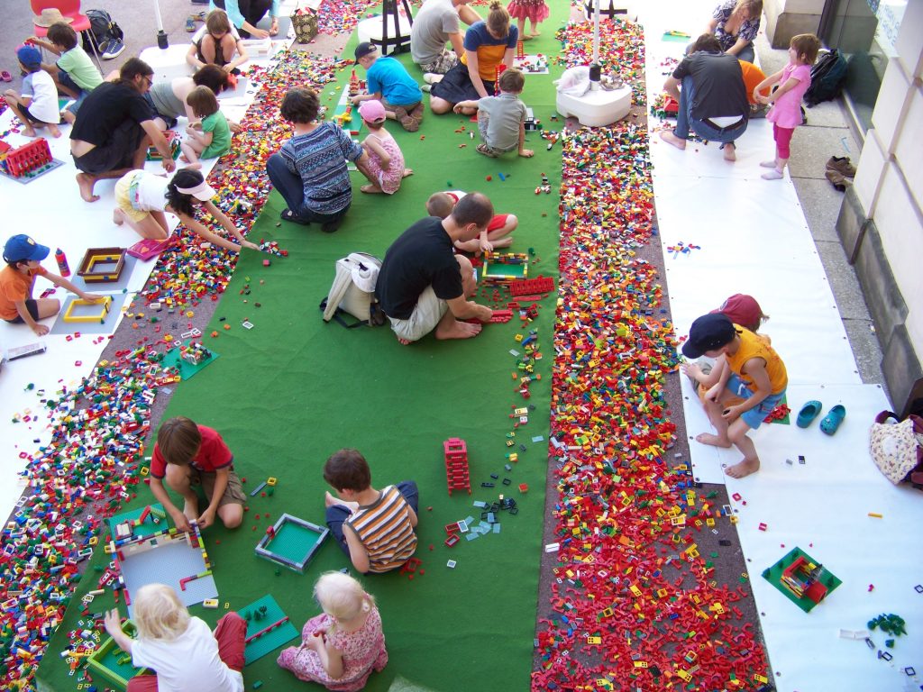 Lots of people erecting buildings using a huge amount of Lego bricks