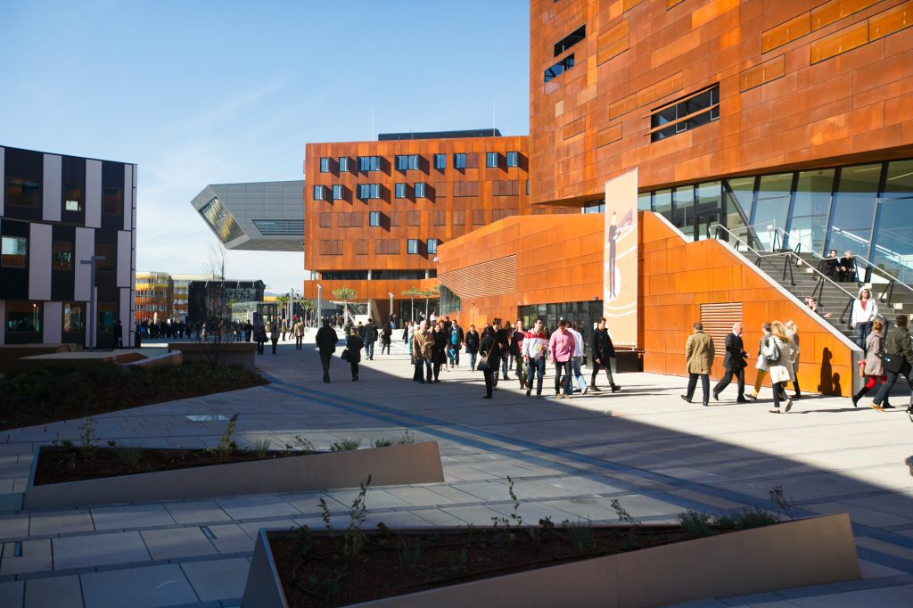 Group strolling between modern university buildings.