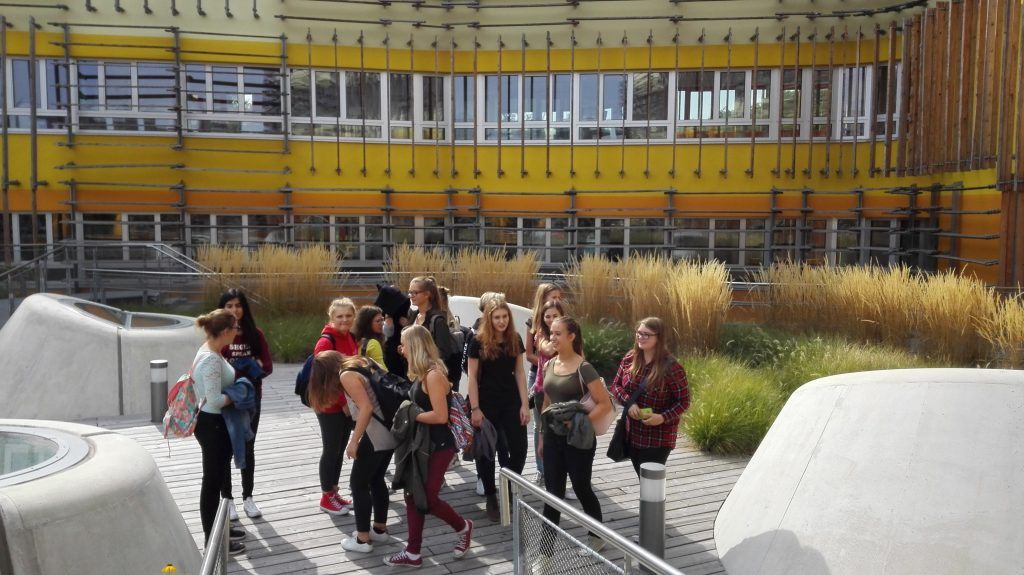 Group of school students in front of a yellow and orange striped building.