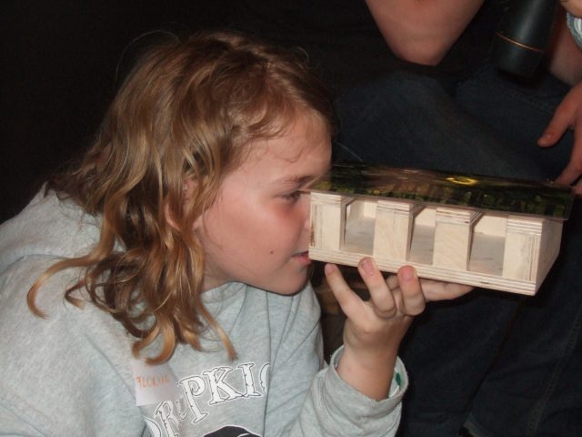 A child looking through a wood model that simulates a lighting situation