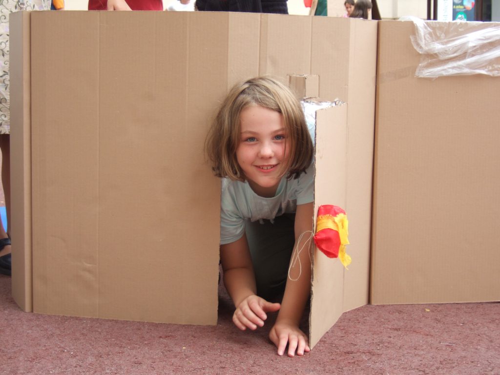 A child clambers out of a cardboard house she built himself