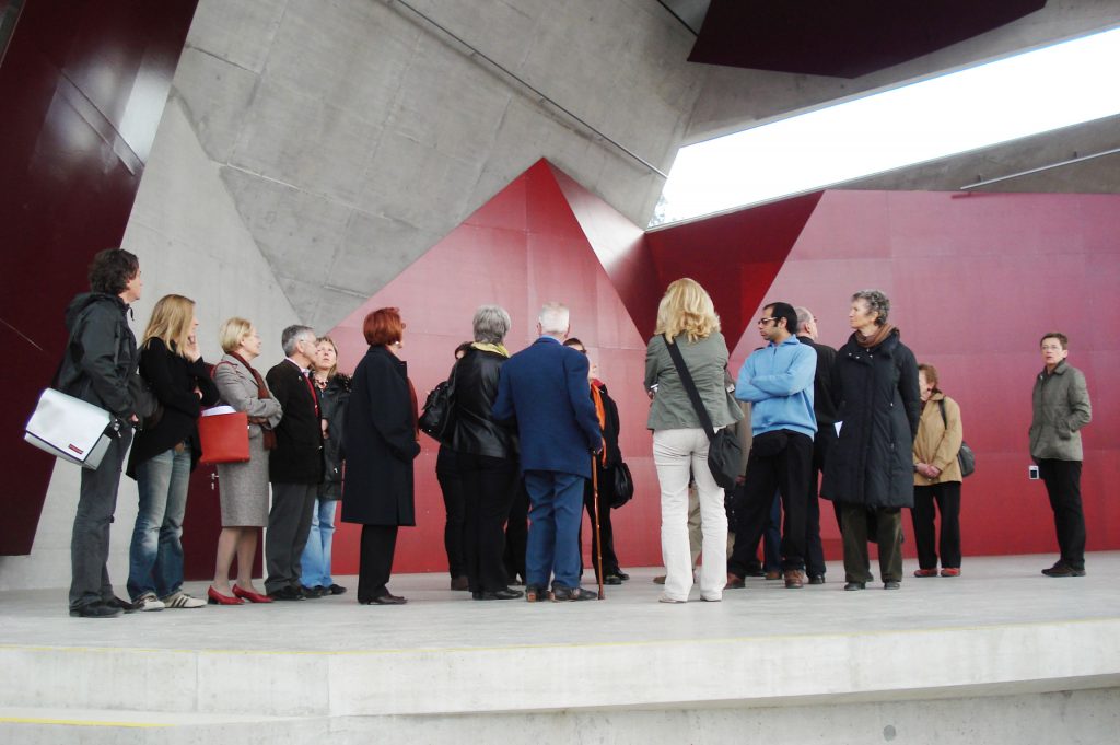 Eine Architektin erläutert ein Gebäude vor einer Gruppe