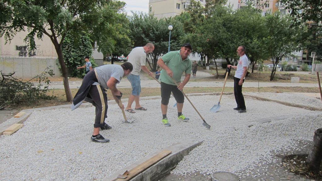 Men using shovels and rakes to spread stones in a bed