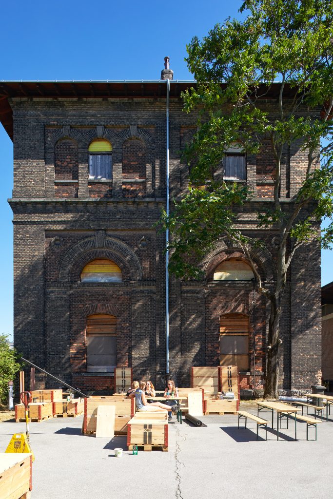 Sitzende Menschen auf Bänken mit Tischen im Hof beim Wasserturm vor der Nordbahn-Halle