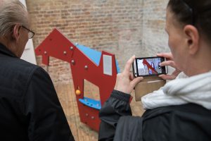 1 Person fotografiert ein Spielplatzmodell in rot-blau