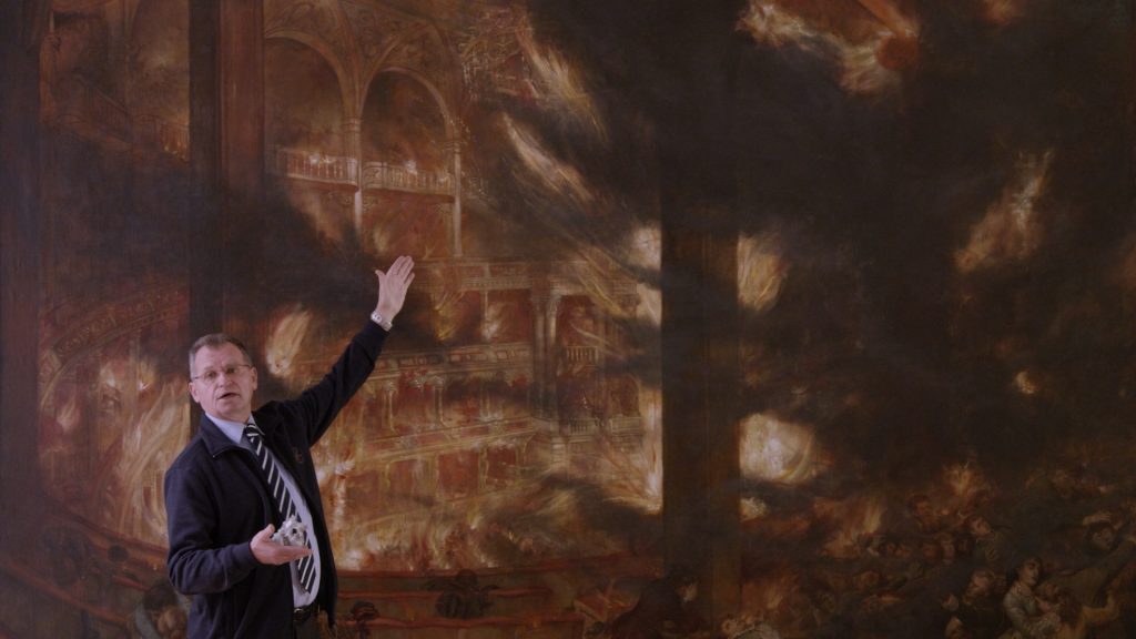 A man points at a painting of the burning Ringtheater in 1881