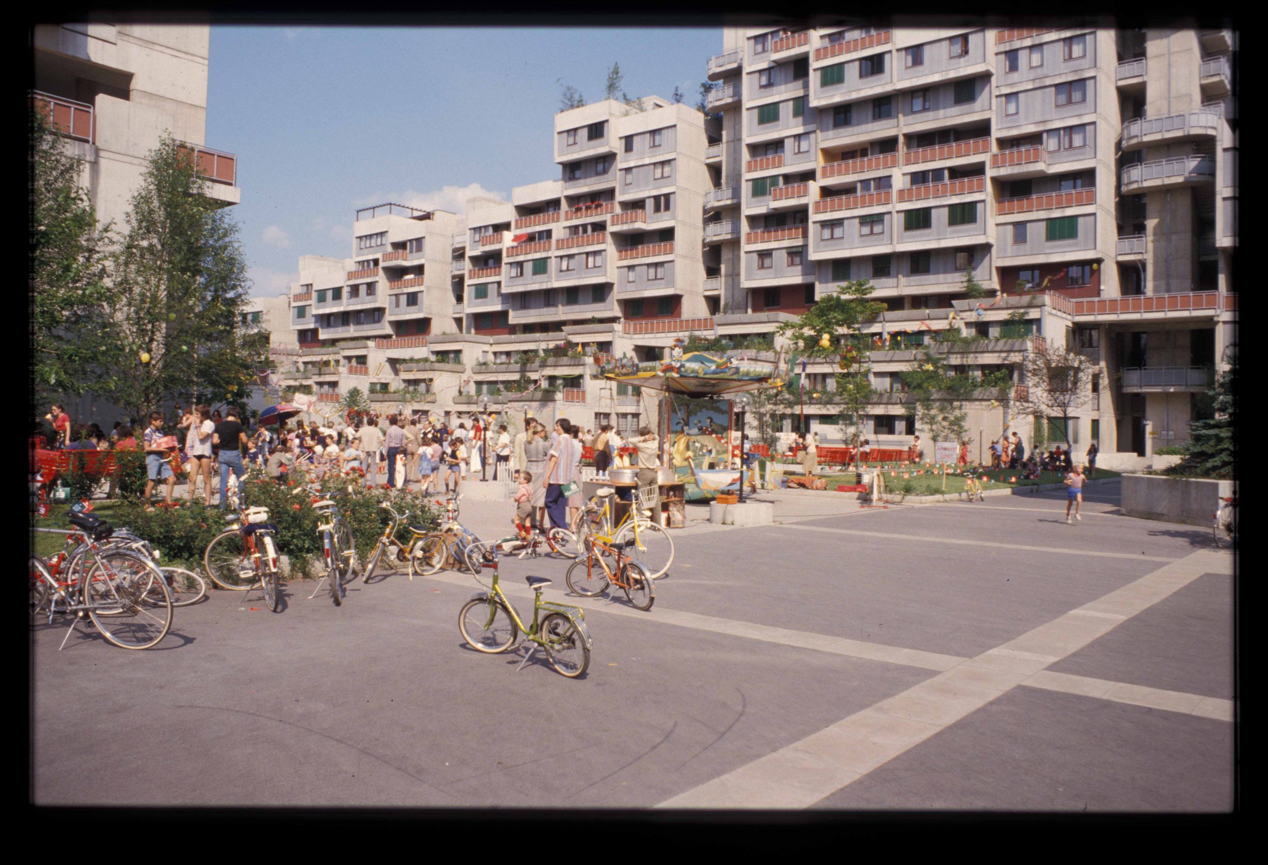 Exterior view, terraced housing estate with bicycles in the foreground and people on a public square