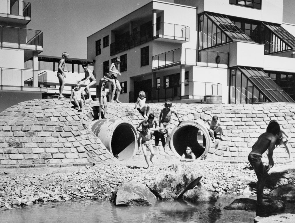 schwarz-weiß Foto mit Kindern in Badebekleidung. Im Hindergrund ein Haus