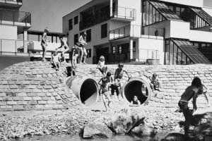 schwarz-weiß Foto mit Kindern in Badebekleidung. Im Hindergrund ein Haus