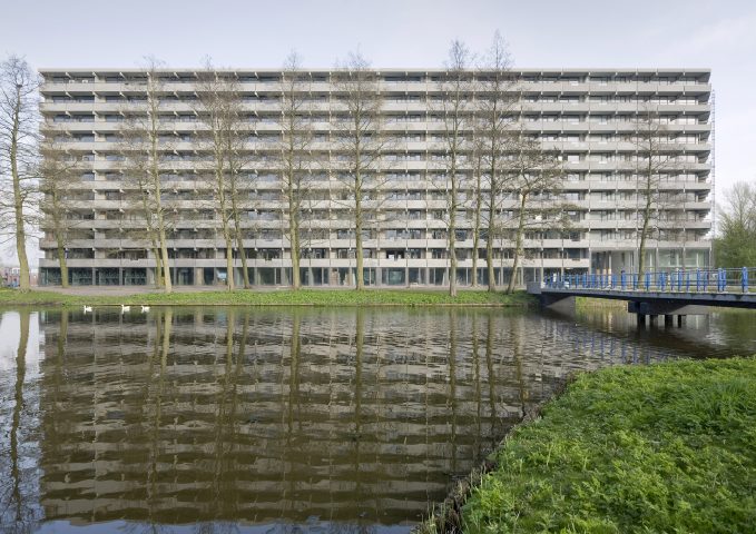 Rechteckiger Wohnblock aus Beton mit Bäumen und See im Vordergrund