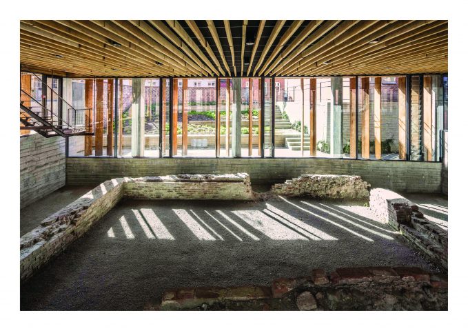 Interior view of a room on the ground floor with wooden ceiling; excavation site with remains of walls; continuous window front with wooden slats