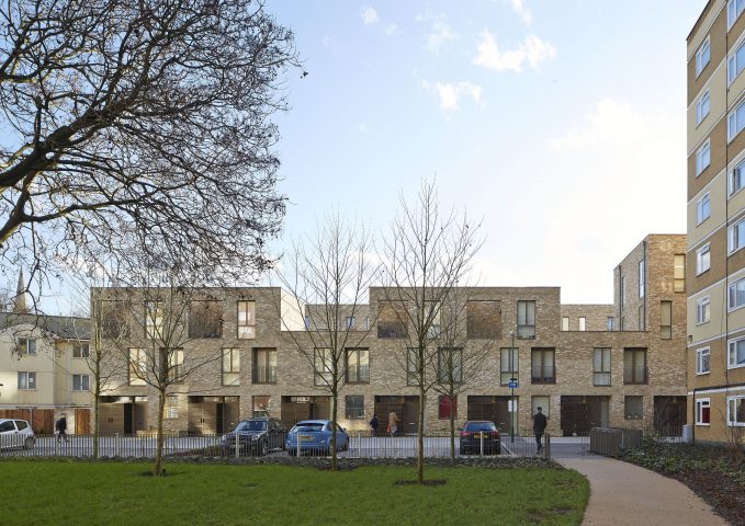 Front view of a two-storey, beige residential building with meadow and trees in the foreground