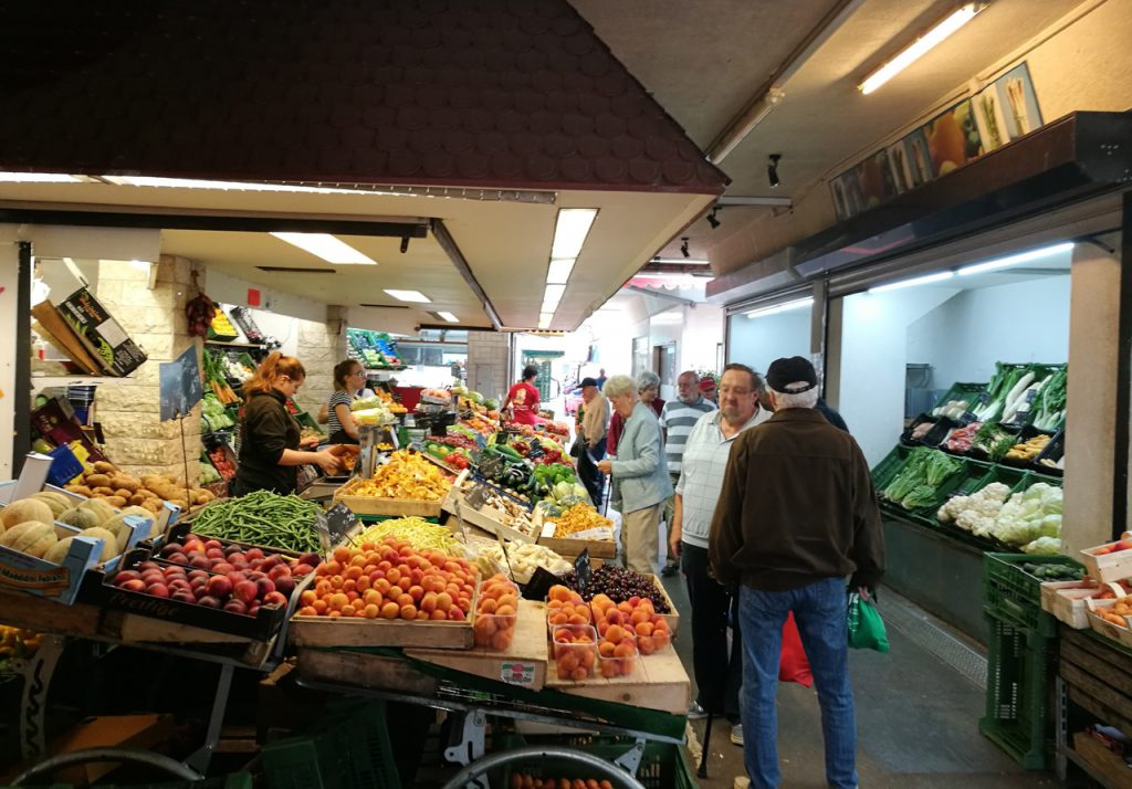 Obst- und Gemüsestand mit Menschen davor in einem Raum.