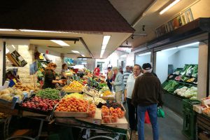 Obst- und Gemüsestand mit Menschen davor in einem Raum.