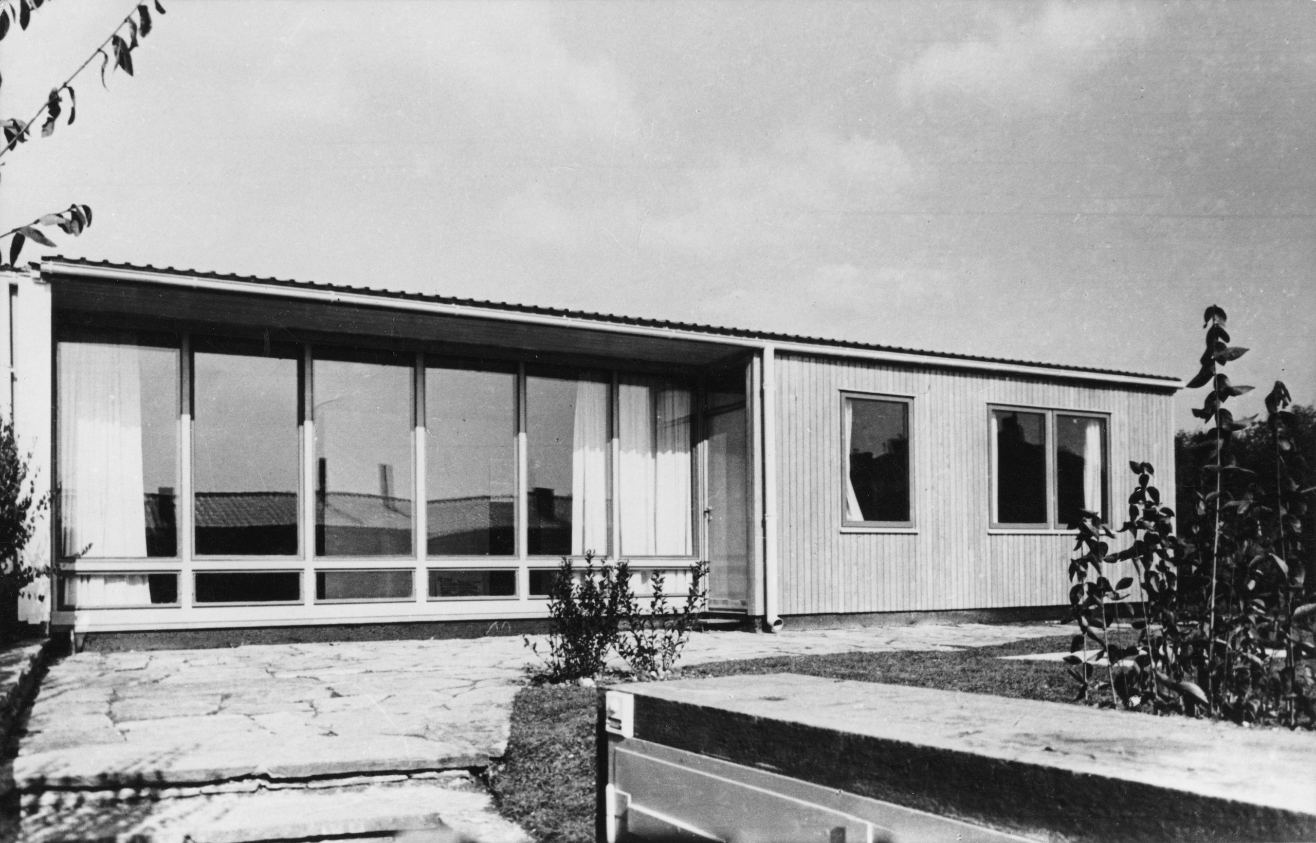 Eingeschoßiges Haus, dessen linke Hälfte der Fassade aus Glas ist, die rechte aus Holz