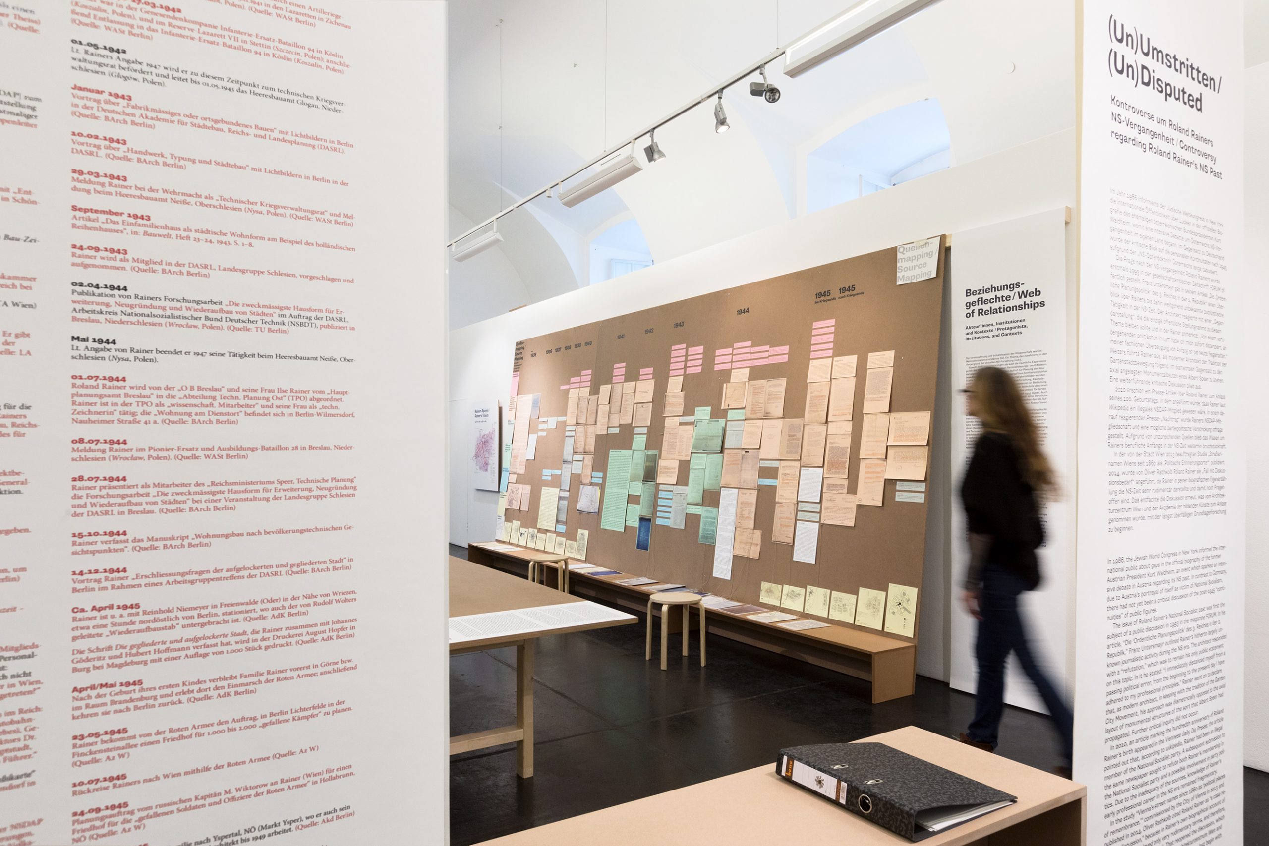 Eine Frau betritt einen Ausstellungsraum, mit Texttafeln an den Wänden