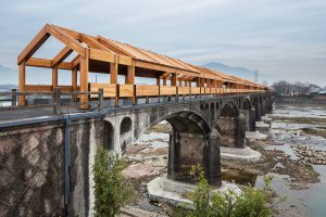 A bridge over a river with old stone viaduct arches and a new wooden structure on top