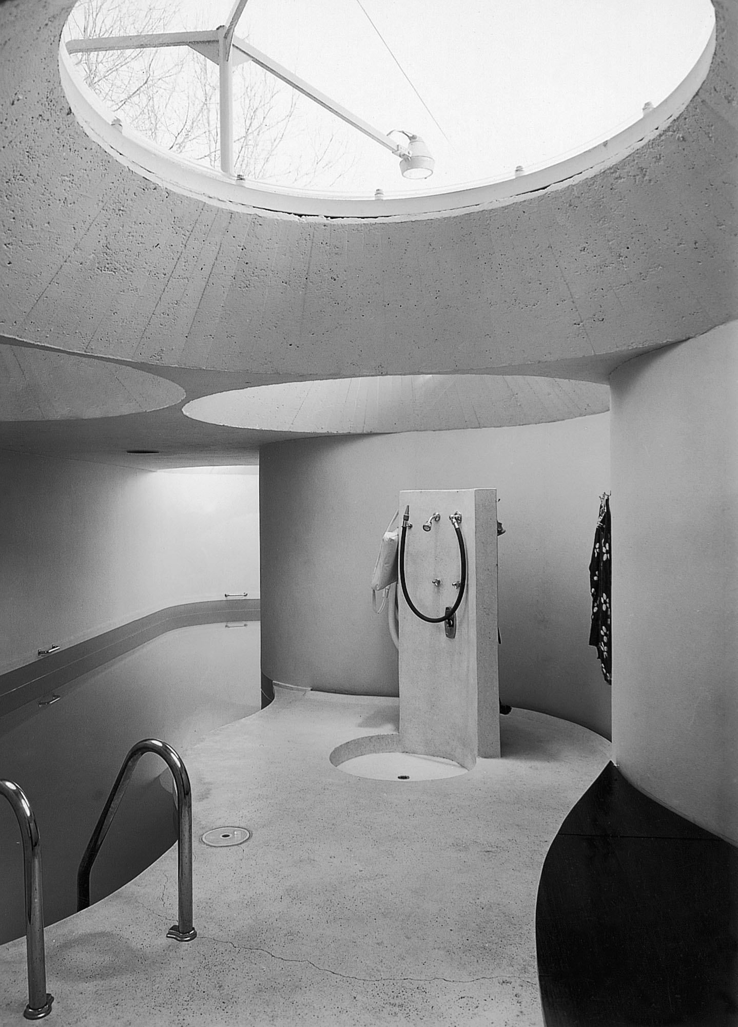 Schwarz-weiß-Innenaufnahme eines Hallenbades mit Dusche und runden Fensteröffnungen in der Decke