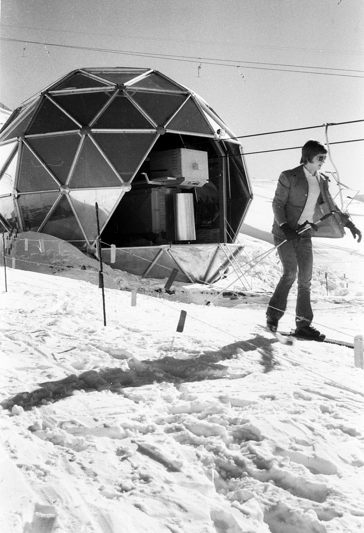 Black and white photo of a spherical building with metal cladding and a skier in the foreground