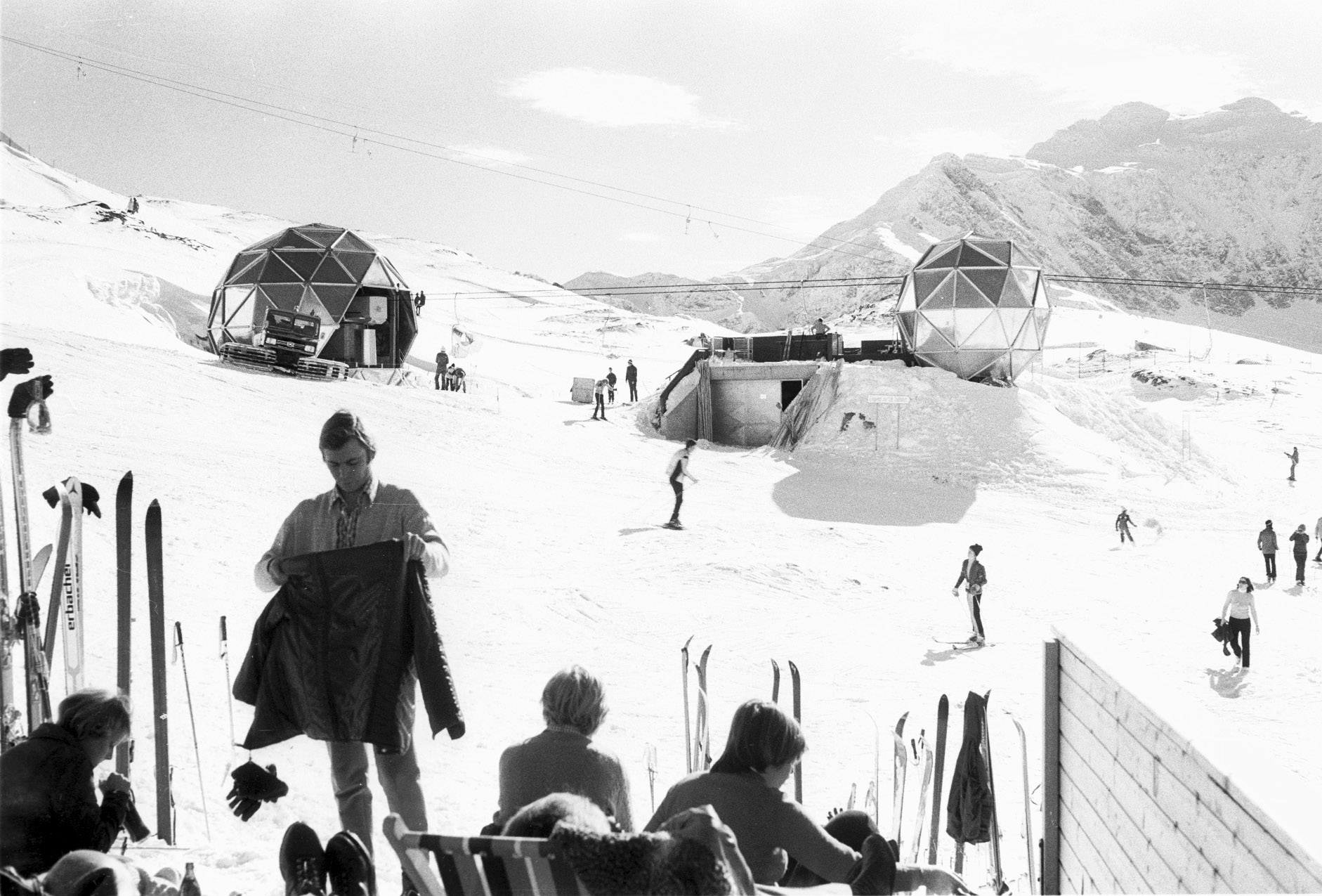 Black and white photograph of two spherical buildings with metal cladding in a winter mountain landscape