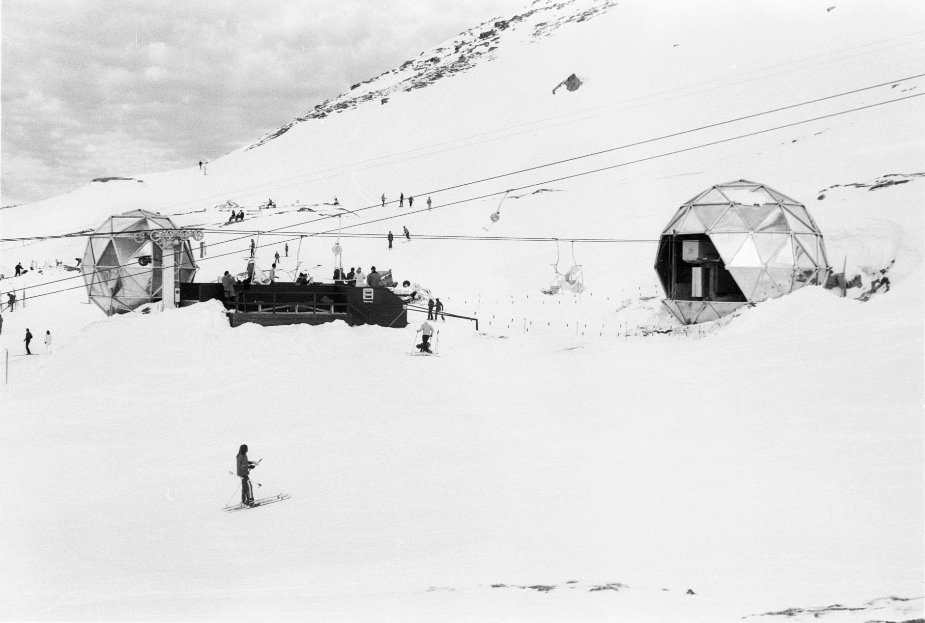Black and white photograph of two spherical buildings with metal cladding in a winter mountain landscape.