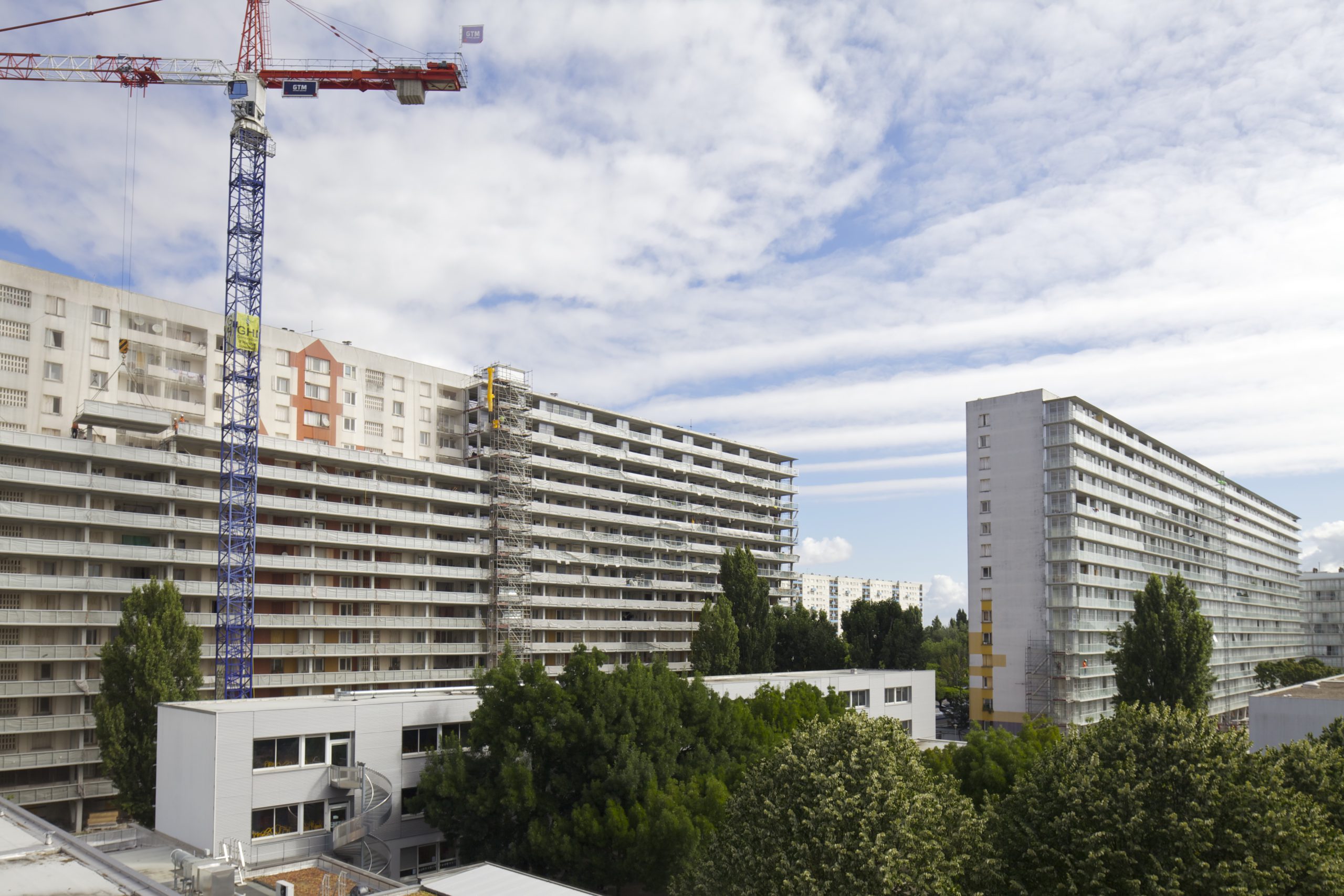 Mehrgeschoßige weiße Wohnblöcke mit einem Kran und Bäumen im Vordergrund