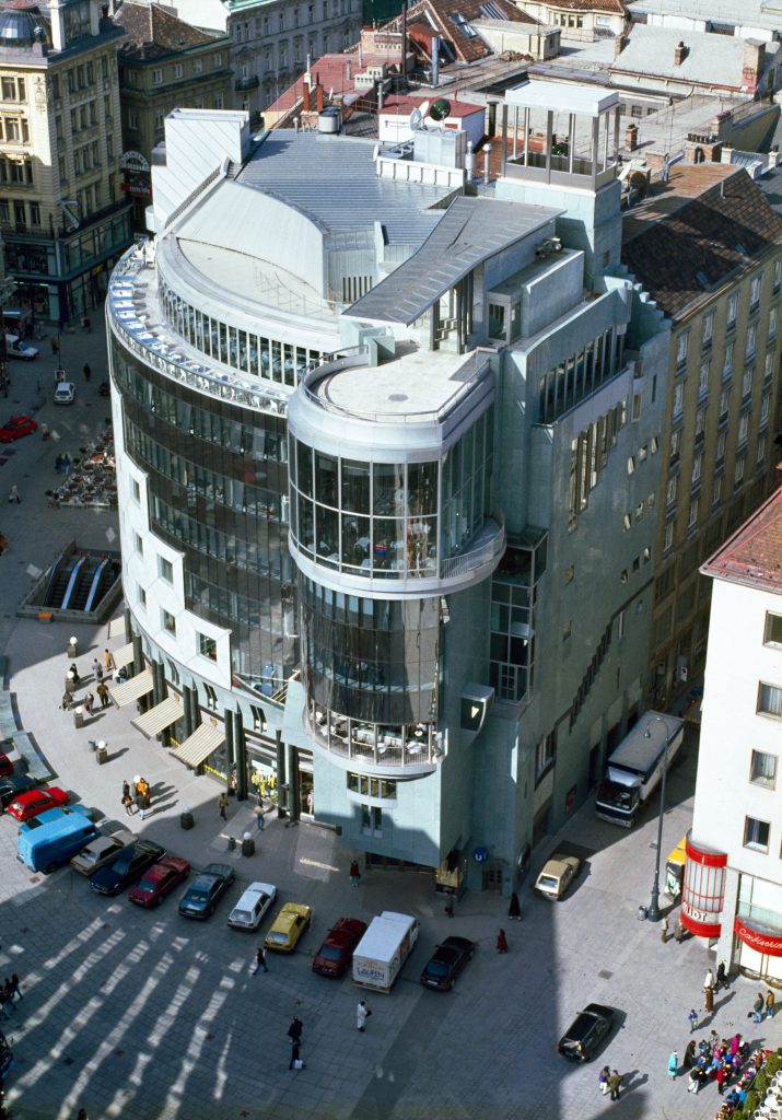 Multi-storey semicircular building with glass facade and parking cars in front of it