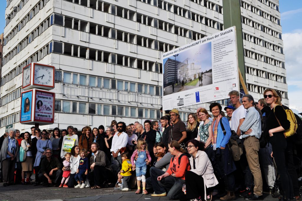 eine Menschengruppe posiert für ein Foto vor eines mehrstöckigen weißen Hochhaus