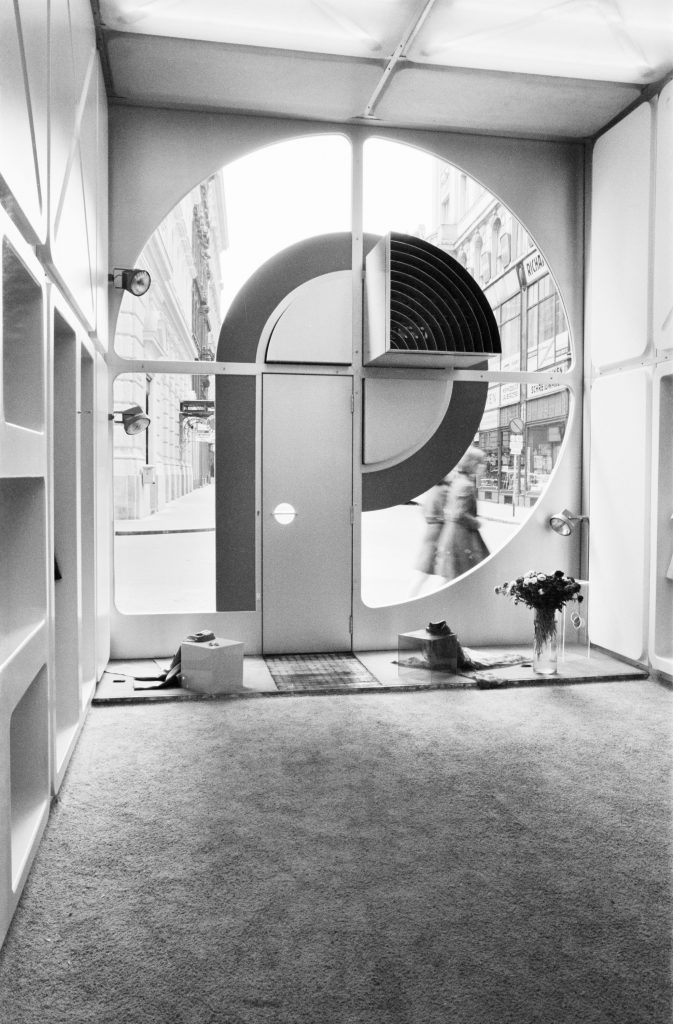 Black and white photograph of an interior with a view through a shop window onto the street.