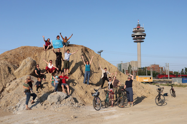 Menschen sitzen auf großem Erdhaufen und Sendeturm in Hintergrund