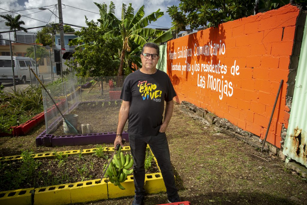 Black dressed man with glasses and bananas in his hand in front of plant beds