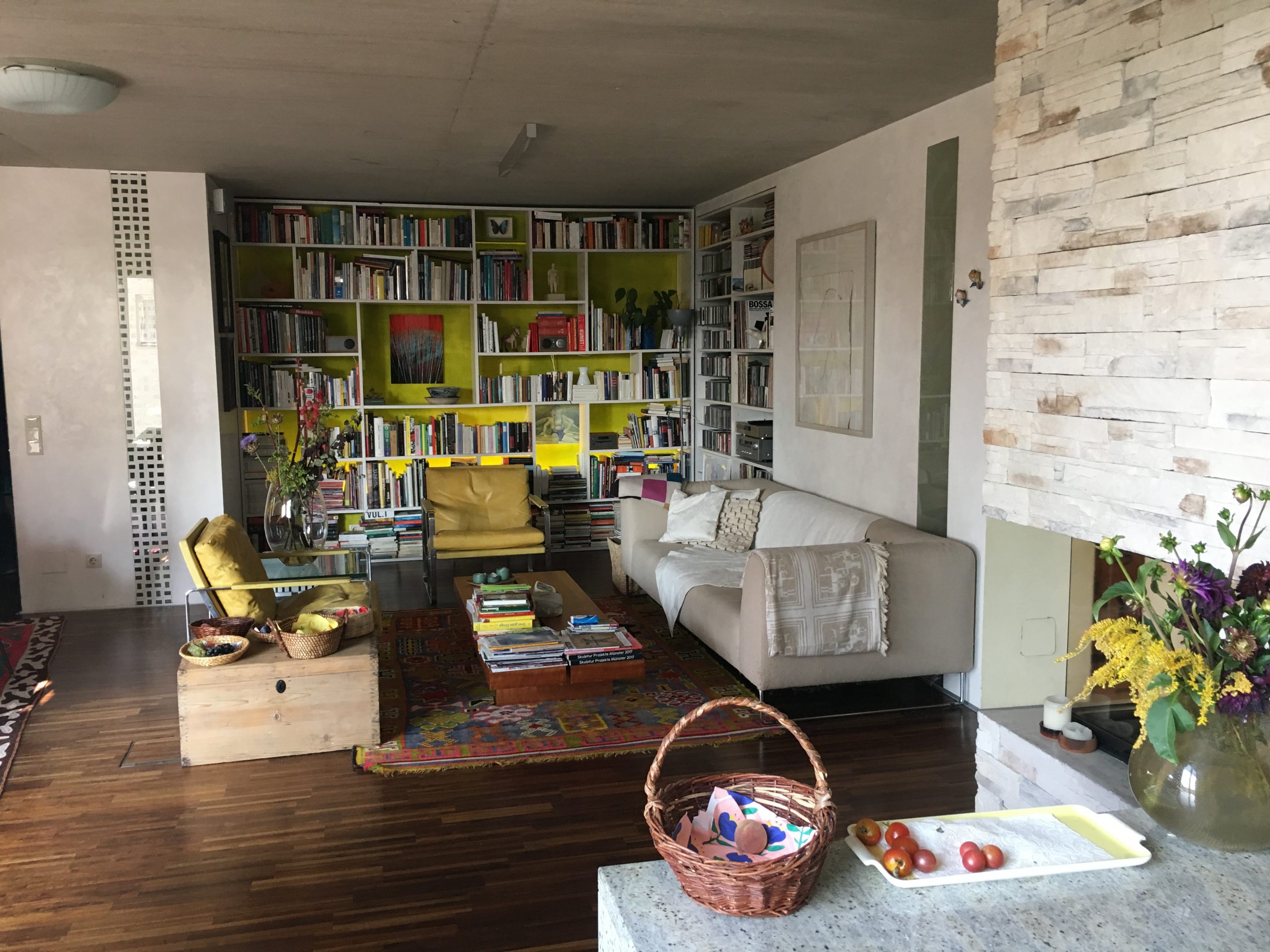 Wohnzimmer mit Couch, Sesseln, Bücherregal und offenem Kamin