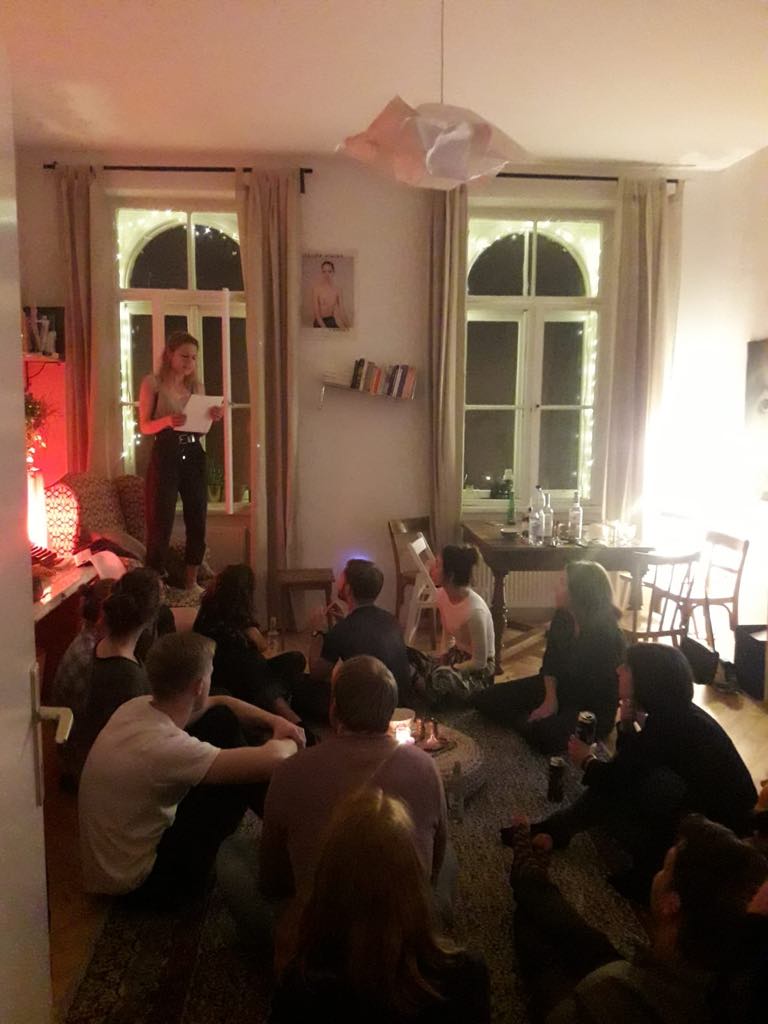 A group of people sitting on the floor of a room with two windows