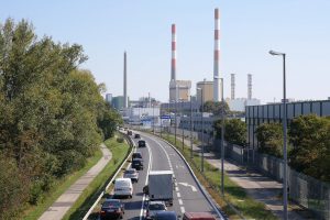 Cars on a multi-lane road and factory chimneys in the background