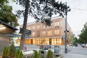 Gebäude mit Holzfassade in dem im untersten Geschoss Licht brennt, davor Bäume