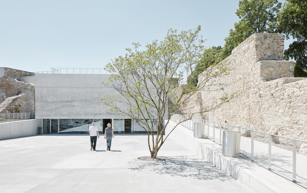 2 persons on q square with small tree and wall on the right