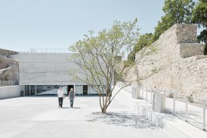 2 persons on q square with small tree and wall on the right