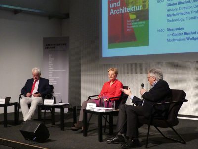 Two men and a woman with a red blouse sitting in front of a big screen