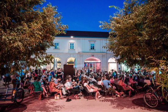 Many people in a courtyard sitting on chairs