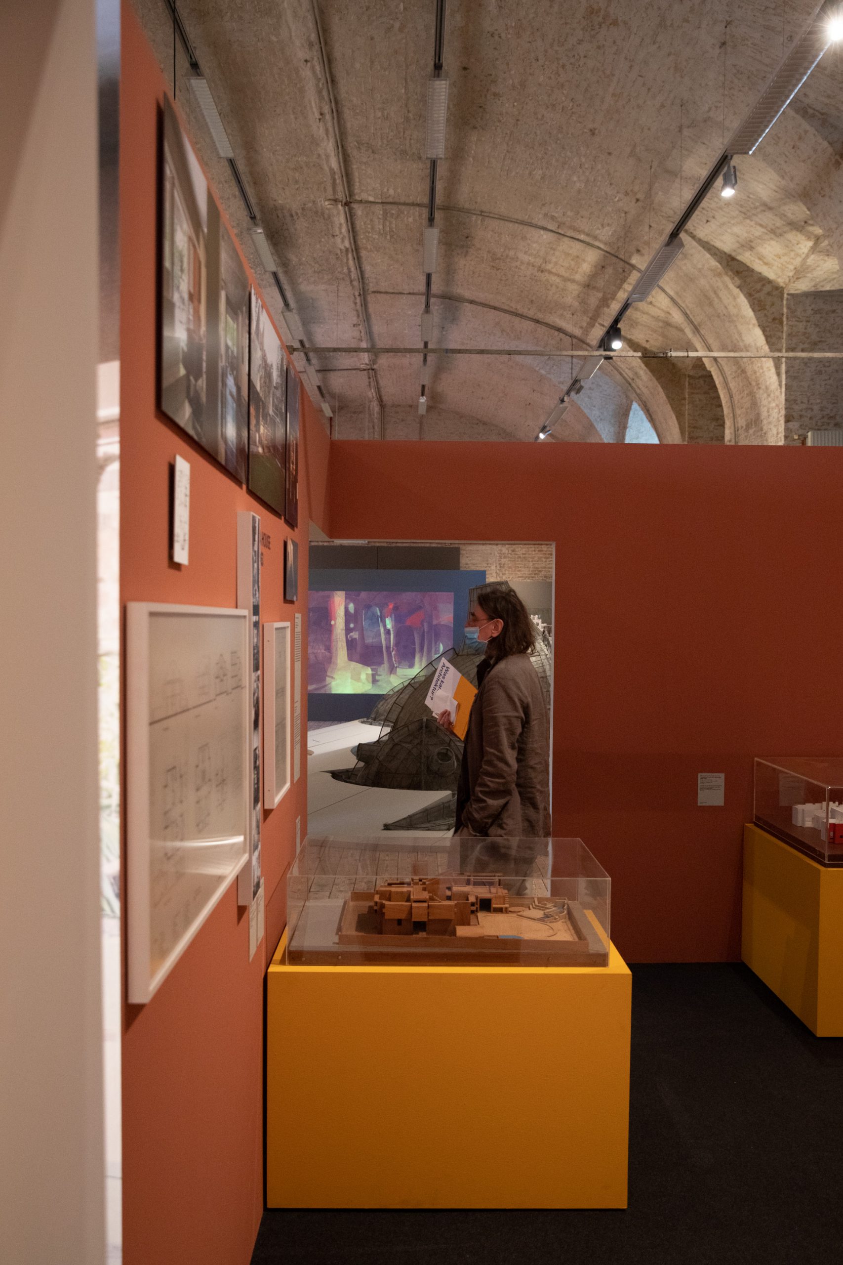 man in front of exhibition wall with photographs and drawings