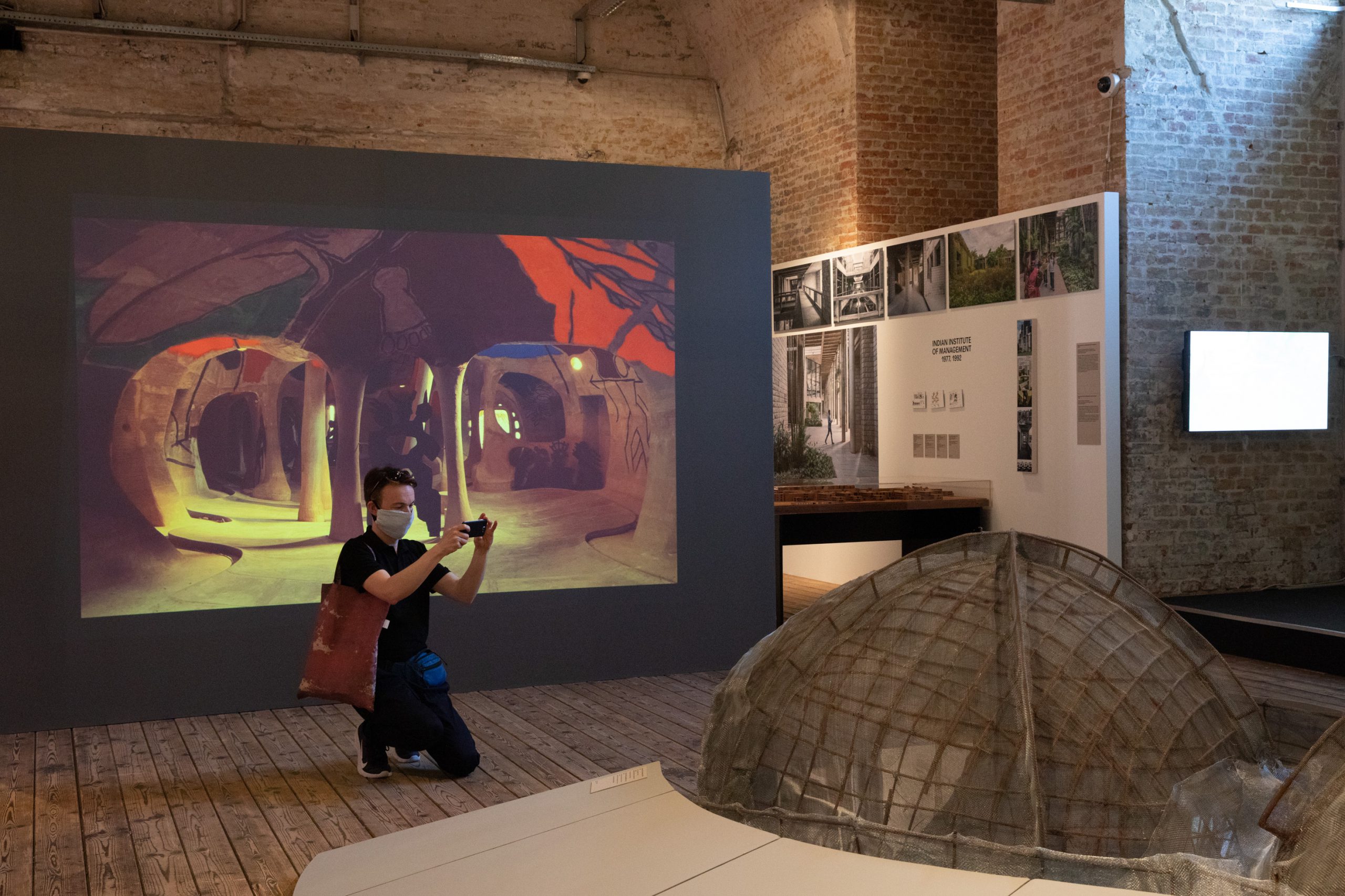 man with mouth-nose protcetion knees in front of huge model and takes a picture of it