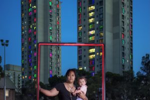 woman with child in her arms in front of skyscrapers holding a red frame