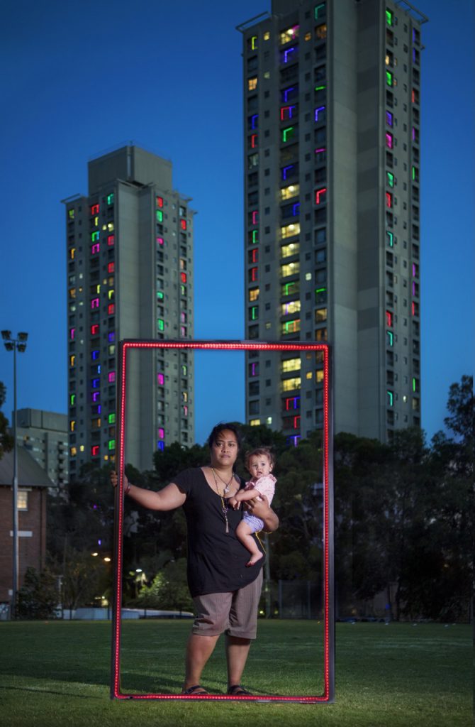 woman with child in her arms in front of skyscrapers holding a red frame