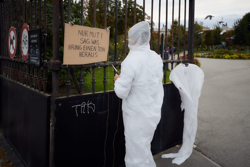 Ein Mensch in weißem Ganzkörperschutzanzug vor Parktor