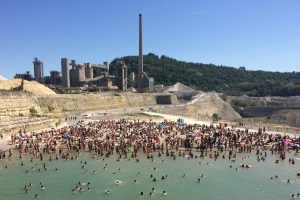 viele Menschen in und am einem See, dahinter eine Fabrik