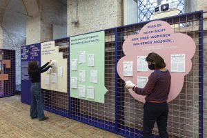 2 women reading in front of a grid wall with colorful boards