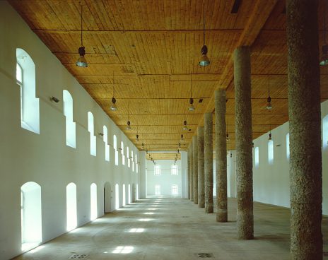 Large elongated interior with windows, columns and wooden ceiling